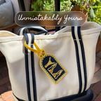 Salty Citrus luggage tag clipped to a navy and cream striped canvas tote bag